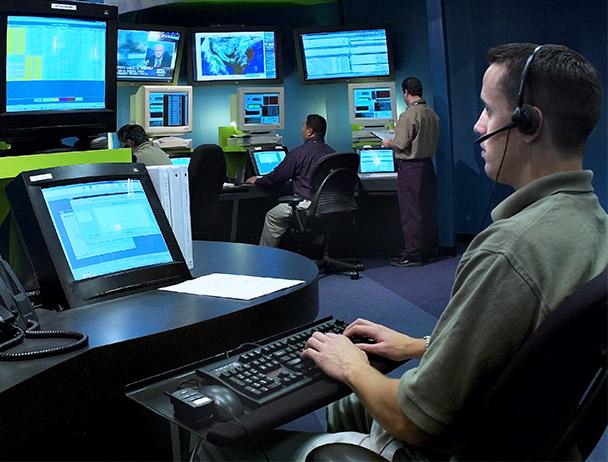 Three Viasat network operations employees monitoring data on computer and TV monitors