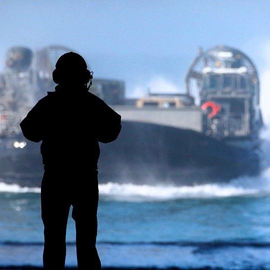 Silhouette of a sailor with a headset using maritime communications to communicate with a LCACs out at sea 